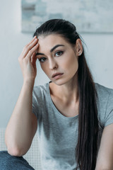 portrait of sad young woman with hand on forehead looking at camera