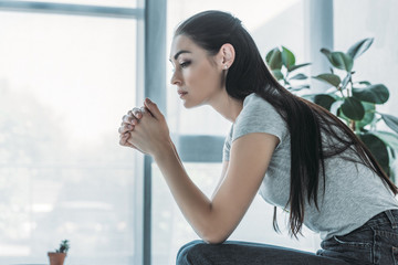 side view of upset brunette woman sitting at home