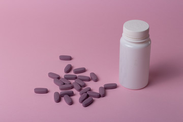 a white box for tablets stands on a pink background, beside lies a bunch of oblong, purple pills.