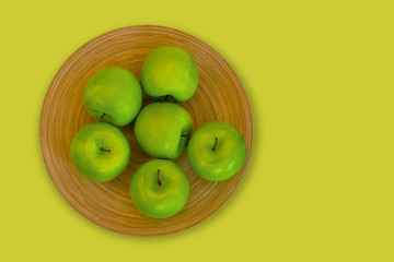 green apples on a brown wooden plate on a green background.