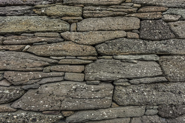 Natural stone wall background with irregular stones in shades of grey with small black and white spots