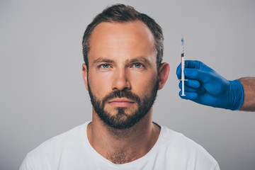 doctor holding syringe in hand and man with alopecia looking at camera isolated on grey
