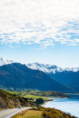 Stunning beautiful view of the road beside Lake Wanaka with alps mountain. Noon scenery with some cloudy and blue sky. nature scene in the countryside with green grassland and agriculture.