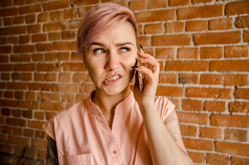 Young beautiful girl in perplexity is talking on the smartphone on a brick wall background