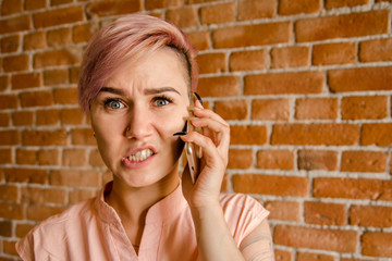 Young beautiful girl in perplexity is talking on the smartphone on a brick wall background