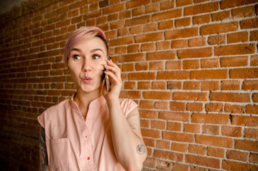 Young beautiful pensive girl is talking on the smartphone on a brick wall background