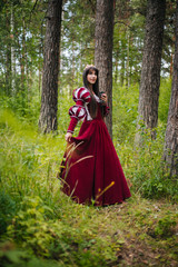 Obraz na płótnie Canvas A beautiful girl with black long hair in a medieval, red dress with a crown on her head walks in the forest. Fairy-tale princess. Fantasy