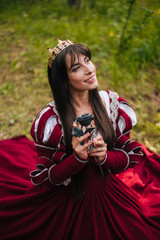 A beautiful girl with black long hair in a medieval, red dress with a crown on her head walks in the forest. Fairy-tale princess. Fantasy