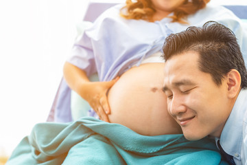 Obraz na płótnie Canvas Husband listening newborn through wife belly. Family awaiting for newborn.