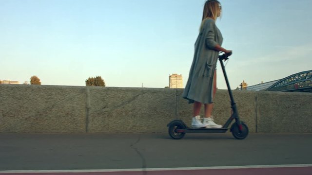 Attractive woman stands, scoots and rides on the electric kick scooter