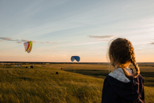 Little girl looks on soaring another paraplanes in sky