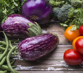 Organic vegetables eggplant, tomatoes, broccoli, green beans for cooking natural vegetarian food on a wooden background.