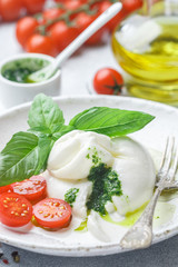 Delicious Italian fresh burrata cheese with arugula salad, cherry tomatoes and olive oil in a white plate. Gourmet snack