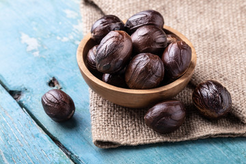 Whole inshell nutmeg nuts in a bowl on blue rustic wooden table.