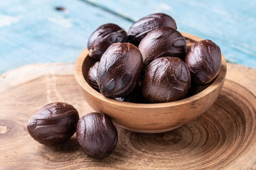 Whole inshell nutmeg nuts in a bowl on blue rustic wooden table.