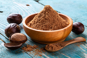 Whole inshell nut, cracked and nutmeg powder in a wooden bowl and spoon on old blue rustic...