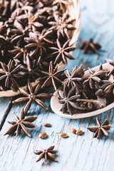 Whole star anise in a basket and spoon with seeds on blue rustic wooden background, indian spice.