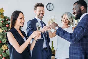 multicultural businesspeople clinking with glasses of champagne with christmas tree on background in office
