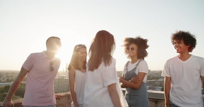 Five multiethnic friends enjoying their time, having summer roof party, talking, cheering closeup 4k