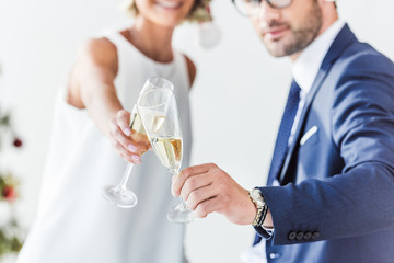 cropped image of businesspeople in santa hats clinking with glasses of champagne in office