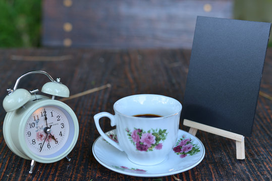 twinbell clock, cup of coffee, and mini blackboard on the wooden table. Image is concept of evening time