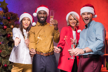 multiethnic businesspeople holding christmas sparklers and glasses of champagne at new year corporate party