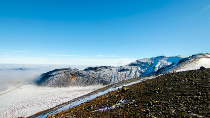 Volcanic rocks landscape above the clouds, climbing from South Crater to Red Crater, view of snow...