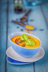 Pumpkin cream soup with pumpkin seeds, pumpkin oil and turmeric on a blue background