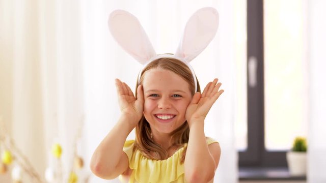 easter, holidays and people concept - happy girl wearing bunny ears headband playing peek a boo game at home