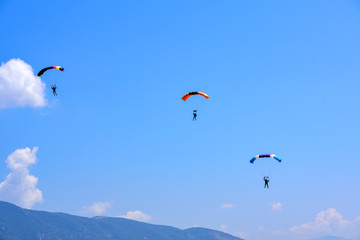 three paratroopers descend against a blue sky