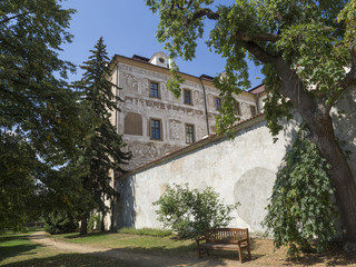 Fototapeta na wymiar Renaissance style castle with Sgraffito decorated facade, park, footpath, green trees garden and wooden bench, sunny summer day