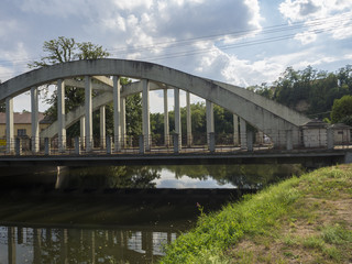 old arc bridge across Jizera river made concrete and metal with view on trees and village summer landscape