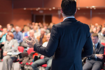 Speaker giving a talk on corporate business conference. Unrecognizable people in audience at...