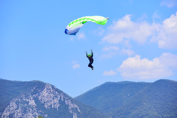 parachutist descends against a blue sky, in the background the mountains