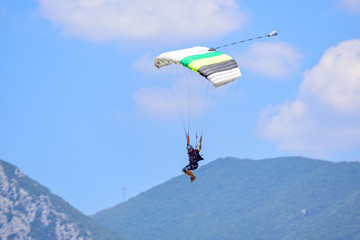 parachutist descends against a blue sky, in the background the mountains