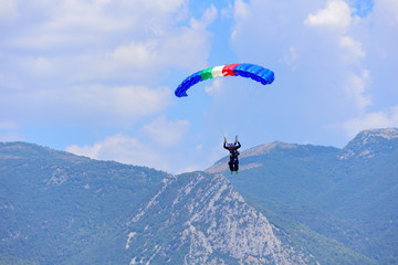 Naklejka na ściany i meble parachutist descends against a blue sky, in the background the mountains