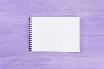 Blank sheet of opened notepad on the violet wooden table