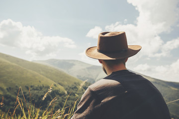 stylish traveler man in hat sitting on top of sunny mountains. travel and wanderlust concept. space...