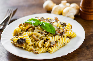 fusilli pasta with mushroom and cream sauce in white plate on a wooden background