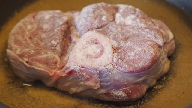 veal shank with marrowbone breaded in flour is fried in a pan