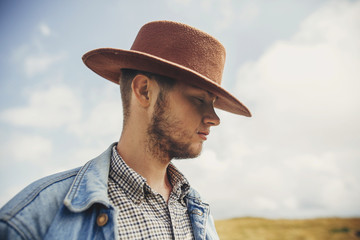 stylish traveler bearded man in hat standing on top of sunny mountains in clouds. space for text....