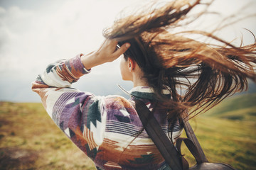 traveler hipster girl with windy hair and backpack, standing on top of sunny mountains. space for...