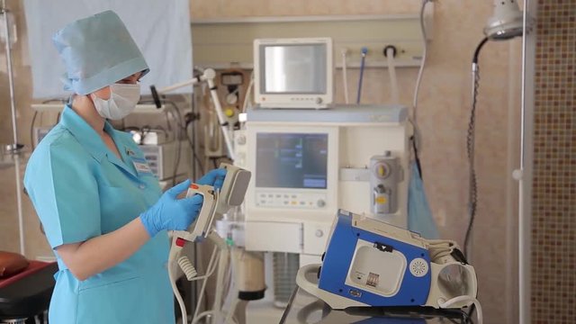 A female nurse prepares a defibrillator for a surgical operation. New medical technologies.4K