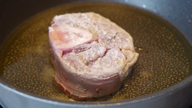 veal meat with marrow bone breaded in flour is fried in a pan
