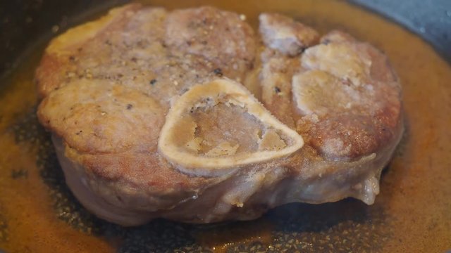 piece of veal meat with marrowbone is fried in a pan in olive oil