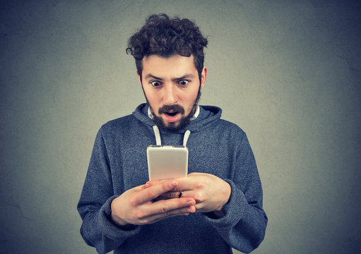 anxious young man looking at mobile phone seeing bad news