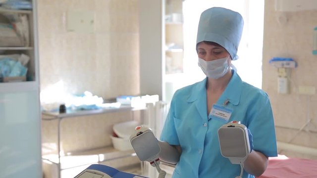 A female surgeon prepares a defibrillator for a surgical operation. New medical technologies.4K