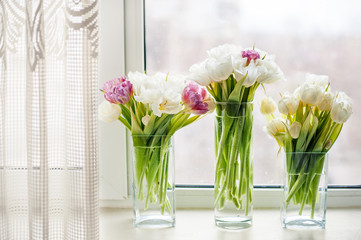 Beautiful gentle bouquets of flowers in glass vases at a window