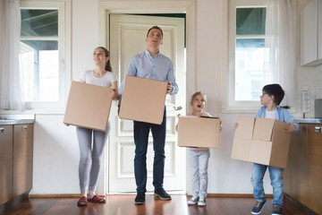 Fototapeta na wymiar Happy family of four carry boxes entering new house, impressed parents and kids bring in cardboard packages moving in to own apartment, surprised mom dad and children relocate with personal belongings