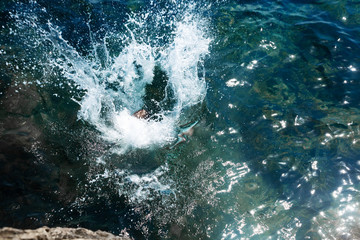 A boy is jumping from the cliff into the sea wiht big water splash on a hot summer day. Holidays on the beach. The concept of active tourism and recreation